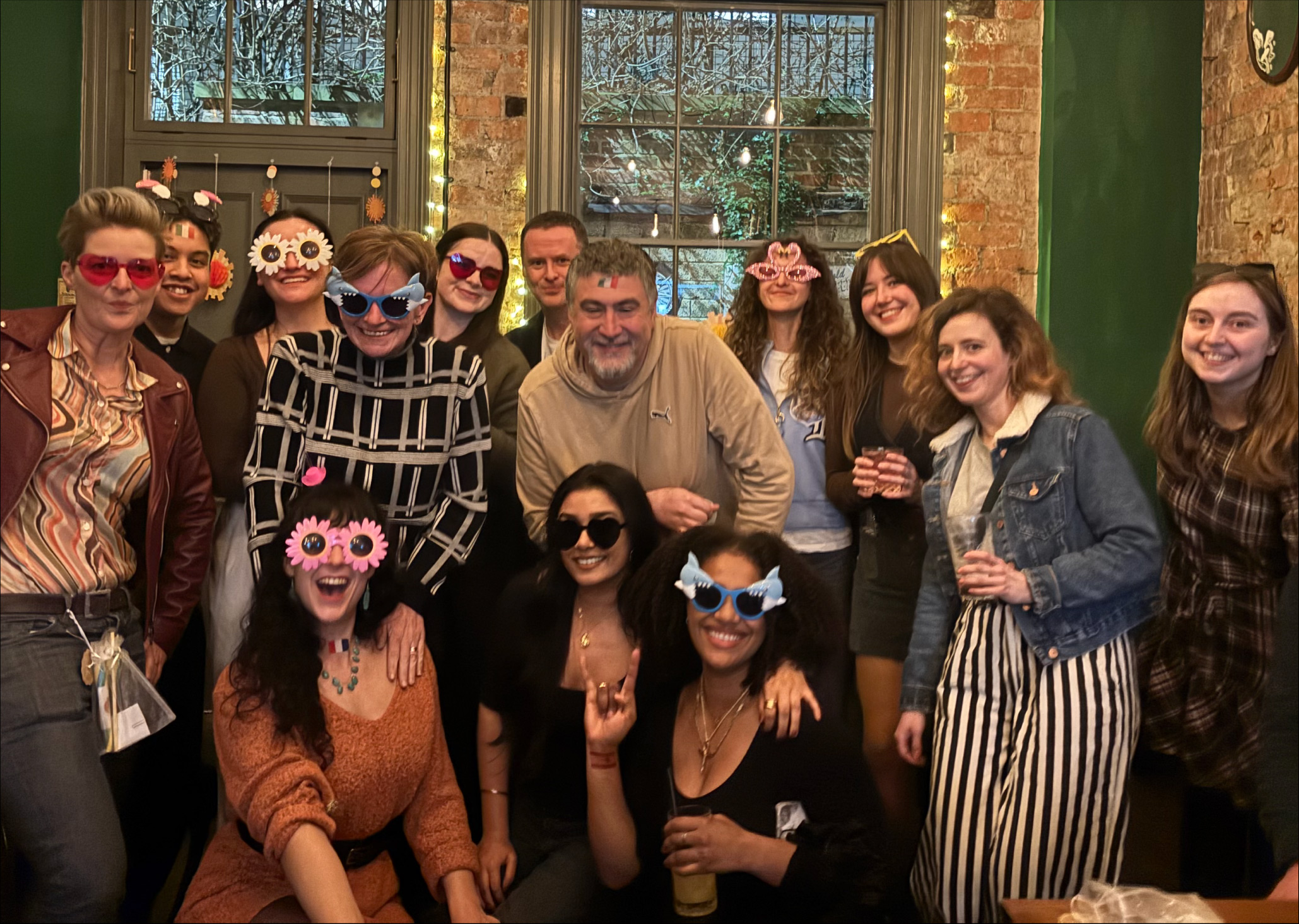 Group of people in a pub, some of which are wearing funny glasses.
